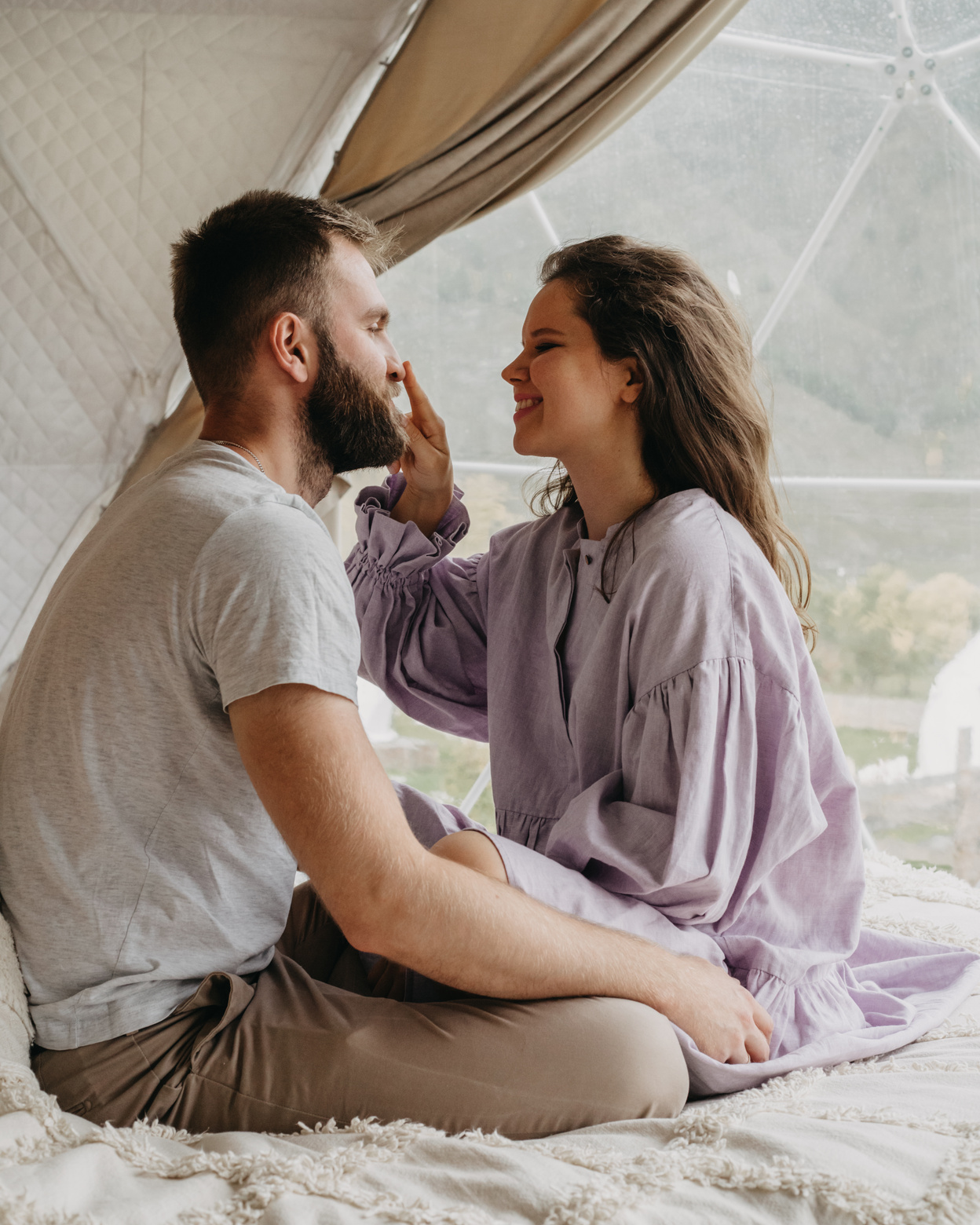 Wife touching husband nose while sitting on bed